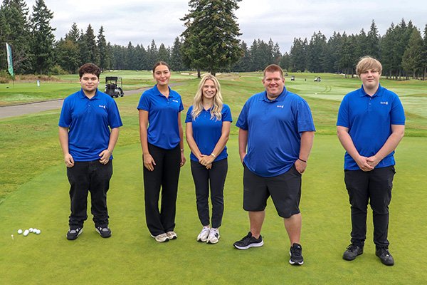 5 staff members in matching blue polo shirts pose for a photo on a golf course