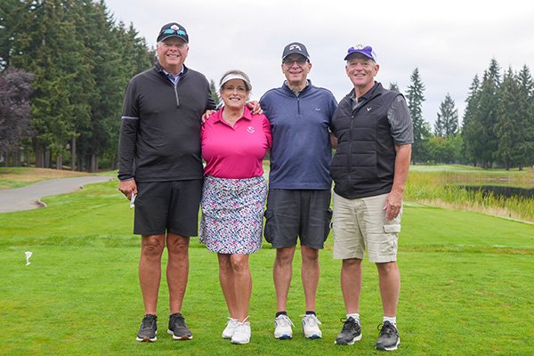3 men and one woman in golf apparel pose for photo on a golf course